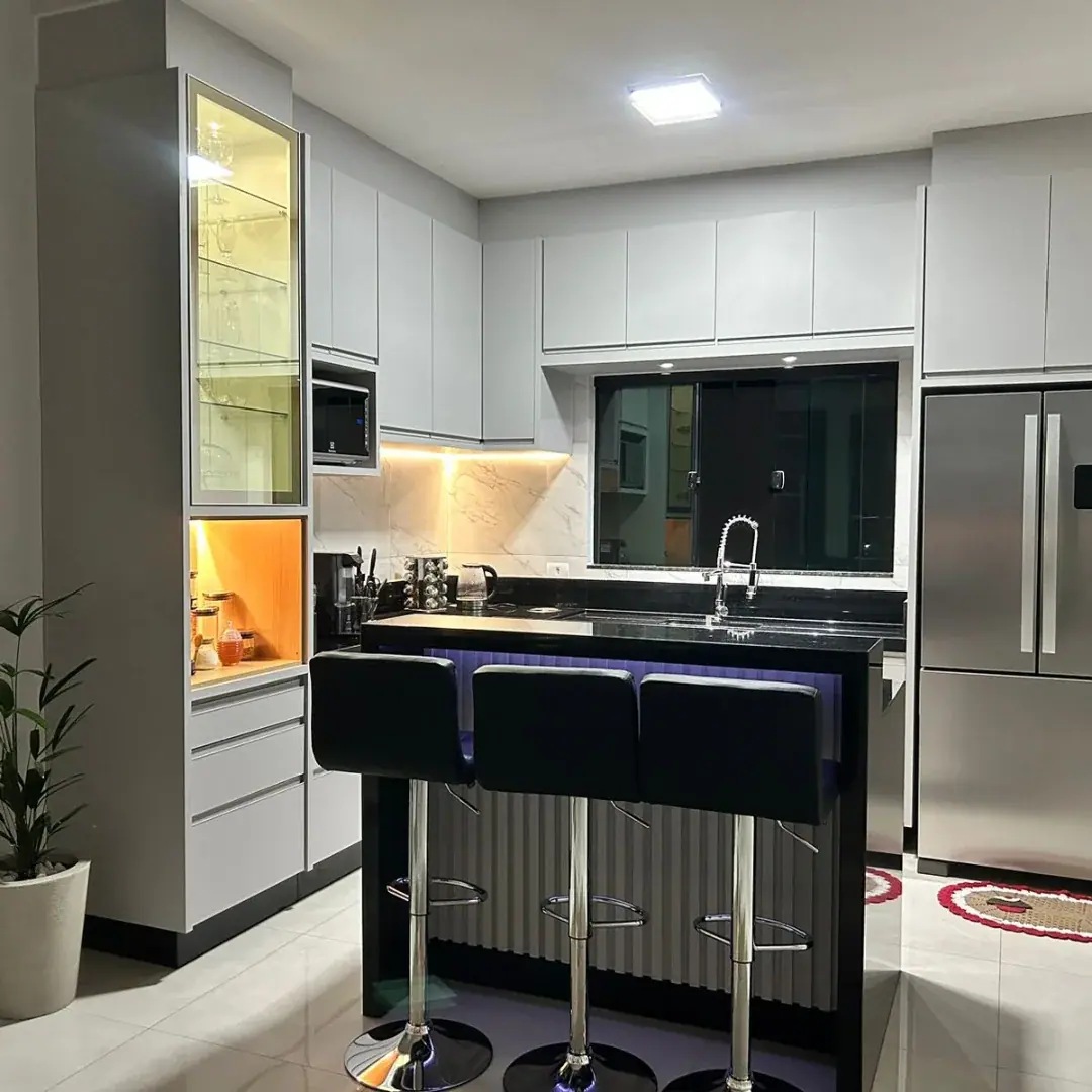 Cozinha planejada cinza claro com ilha preta, cristaleira iluminada e nicho para micro-ondas