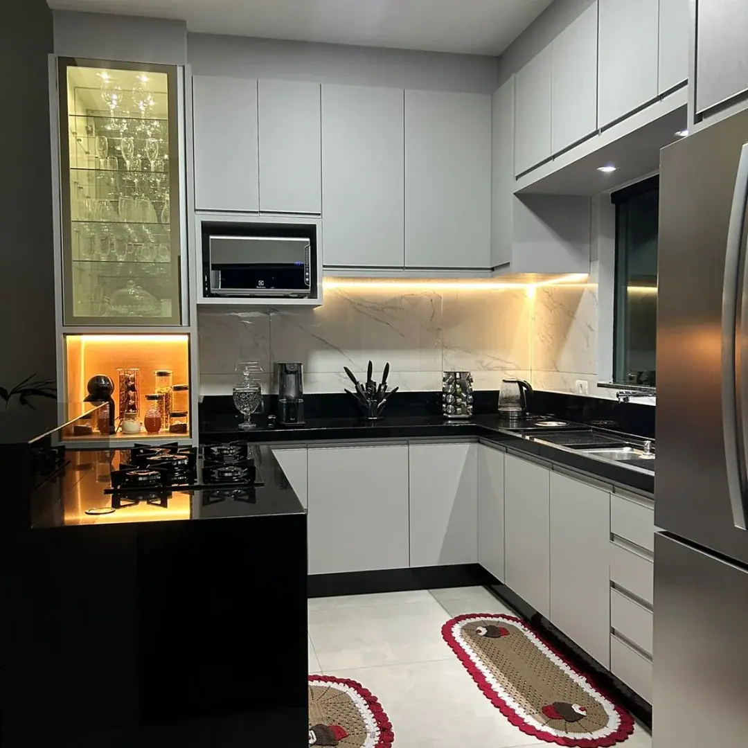 Cozinha planejada em L cinza claro com bancada preta, cooktop na península e cristaleira com LED